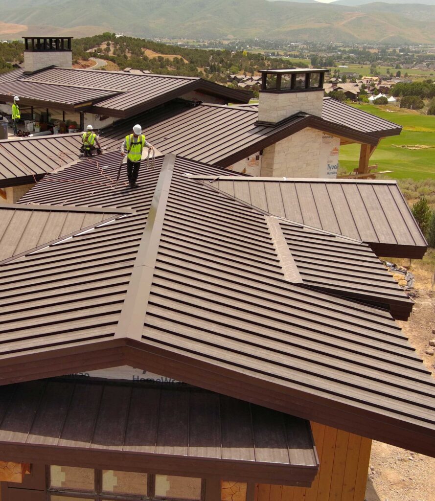 Roofing crew installing a metal roof on a Utah home with safety gear and mountain views in the background